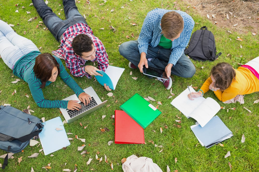 High angle view of young college students using laptop while doing homework in the park